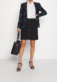 Rutig kavaj med svarta slag, vit skjorta, svart knälång kjol med guldknappar, svart handväska och svarta sandaler med remmar.