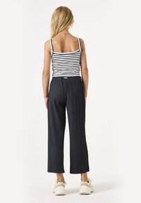 Zwarte, geplooide wijde broek met een elastische tailleband, gecombineerd met een zwart-wit gestreept hemdtopje en lichte sneakers.