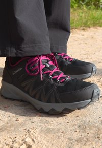 Svart sportsko med rosa snører, mesh overdel, teksturerte sidepaneler og en robust grå såle, egnet for utendørsbruk.