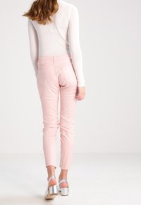 Pantalones rosas ajustados con una textura suave y una cinturilla de talle medio, combinados con sandalias plateadas de tacón con un diseño grueso.