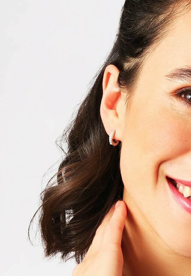 Orecchini a cerchio in argento con una finitura texturizzata e piccoli accenti decorativi, indossati all'orecchio di una persona con capelli scuri.