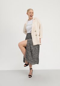 Kremfarvet hørblazer med guldknapper, hvid t-shirt med grøn tekst og sort ankel-lang nederdel med hvidt abstrakt mønster. Sorte sandaler med hæl.