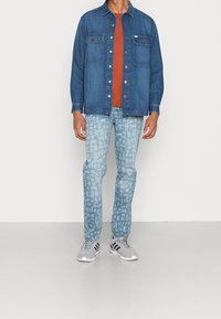 Camisa de mezclilla, dos bolsillos en el pecho, color azul; camiseta naranja debajo; jeans azul claro con estampado; zapatillas grises con detalles en negro y rojo.