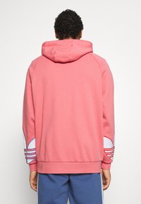 Sudadera rosa con capucha ajustable y puños acanalados. Presenta detalles en blanco en las mangas con líneas curvas y una tela suave y texturizada.