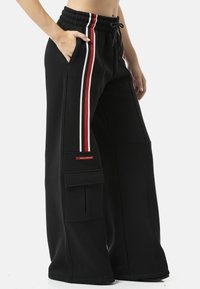 Zwarte sweatpants met wijde pijpen en een tailleband met trekkoord, voorzien van rode en witte zijstrepen en een zijzak met klep.