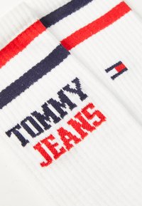 Weiße Rippensocken mit roten und blauen Streifen am Bund. "TOMMY" in Marineblau und "JEANS" in Rot, plus ein kleines Logo in Marineblau, Rot und Weiß.