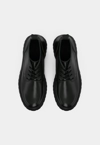 Čierne kožené topánky s hladkým povrchom, dizajnom na šnurovanie, zaoblenou špičkou a hrubou gumovou podrážkou. Obsahujú pútko pre jednoduchšie obúvanie.