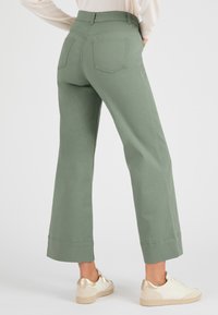 Hoog-waist, wijde broek in olijfgroen, met twee achterzakken en een gecropte zoom. G gedragen met lichtgekleurde sneakers.