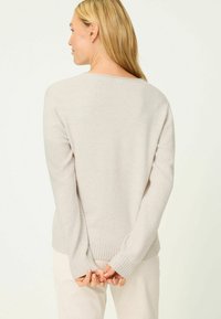 Beiger Pullover aus weichem Material mit Rundhalsausschnitt, gerippten Bündchen und Saum. Die Rückansicht zeigt lange Ärmel und eine lockere Passform.