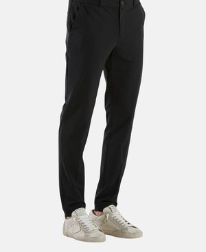 Pantalons noirs ajustés, avec des poches latérales, un devant plat et une texture lisse. Associés avec des baskets beiges.