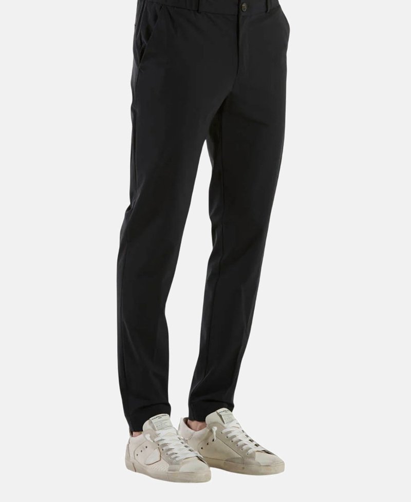 Pantaloni neri slim fit, con tasche laterali, frontale piatto e una texture liscia. Abbinati a sneakers beige.