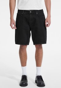 Pantaloni scurți din denim negru cu croială dreaptă, cinci buzunare și închidere cu buton metalic. Prezintă un tiv curat și o textură subtilă.