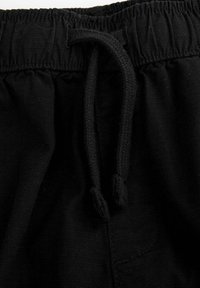 Czarny pas zsuwany z materiału o fakturze, z widocznymi szwami i dwoma związanymi końcami. Materiał wydaje się miękki i elastyczny.