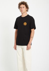 Sort bomulds t-shirt med et gult solstrålegrafik på venstre bryst. T-shirten har en klassisk pasform og korte ærmer.