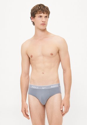 Gray Nike briefs with a white elastic waistband featuring a logo. Smooth fabric, low-rise cut, form-fitting design, minimalistic style.