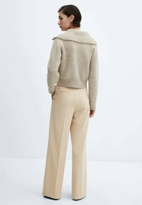 Beige gebreide trui met een brede kraag, gecombineerd met hooggesneden beige broek. Soepele textuur, op maat gemaakte pasvorm en minimalistisch ontwerp.