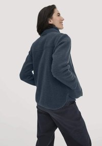 Donkerblauwe fleecejack met een hoge kraag, een losse pasvorm, raglanmouwen en een afgeronde zoom. Vriendelijke textuur en minimale stikdetails.