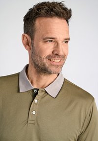 Olivgrön polo-shirt med en ljusgrå strukturerad krage, tre knappar och en slät tygfinish. Har en avslappnad passform.