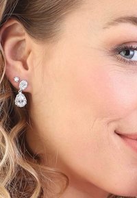 Silberfarbene Ohrringe mit drei klaren Edelsteinen: einem kleinen sternförmigen Stecker, einem größeren ovalen Anhänger und einem tropfenförmigen Akzent.