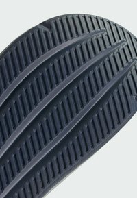 Suela de zapato de goma negra con estrías y ranuras texturizadas para tracción. Los bordes redondeados y un acabado suave caracterizan el diseño.