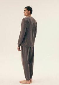 Szary zestaw odzieży do relaksu składający się z bluzki z długim rękawem i luźnych spodni, wykonany z miękkiego materiału z prążkowanymi mankietami i pasem.