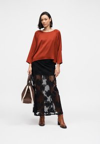 Haut rouge ample à manches longues, associé à une jupe noire en dentelle ornée de motifs floraux. Sac à main marron et bottines.