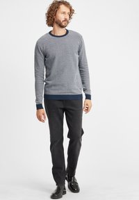 Maglione da uomo a maglia grigio con un motivo testurizzato, colletto tondo blu navy e polsini blu navy; abbinato a jeans neri a gamba dritta e stivali neri.