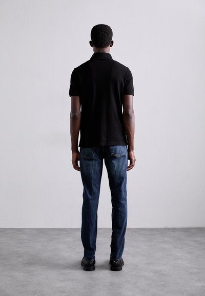 Svart polo t-shirt med korta ärmar, i kombination med blå denimjeans. Betraktad bakifrån, visar en enkel design och solida färger.