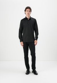 Cămașă din bumbac negru cu mâneci lungi, cu închidere la față cu nasturi și guler standard. Purtați cu pantaloni negri asortați și pantofi negri lucioși.