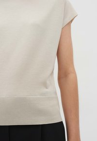 Top beige a maniche corte con una texture liscia, orlo a coste e vestibilità rilassata, progettato per comfort e versatilità.