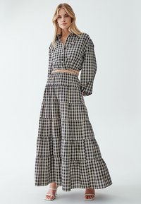 Čiernobiely károvaný dvojdielny outfit, ktorý pozostáva z skráteného košele s dlhými rukávmi a vrstvenej maxi sukne. Textúrovaná tkanina.