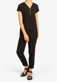 Top nero a maniche corte con scollo a V e dettaglio con zip, abbinato a pantaloni neri affusolati e sandali neri massicci. Tessuto liscio e leggero.
