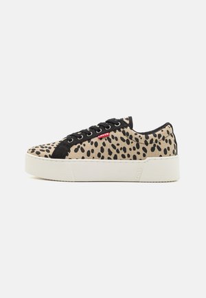 Beiga sneakers med svart leopardmönster, svarta mockadelar, rund tå, vit gummisula och en framträdande röd logotagg på sidan.