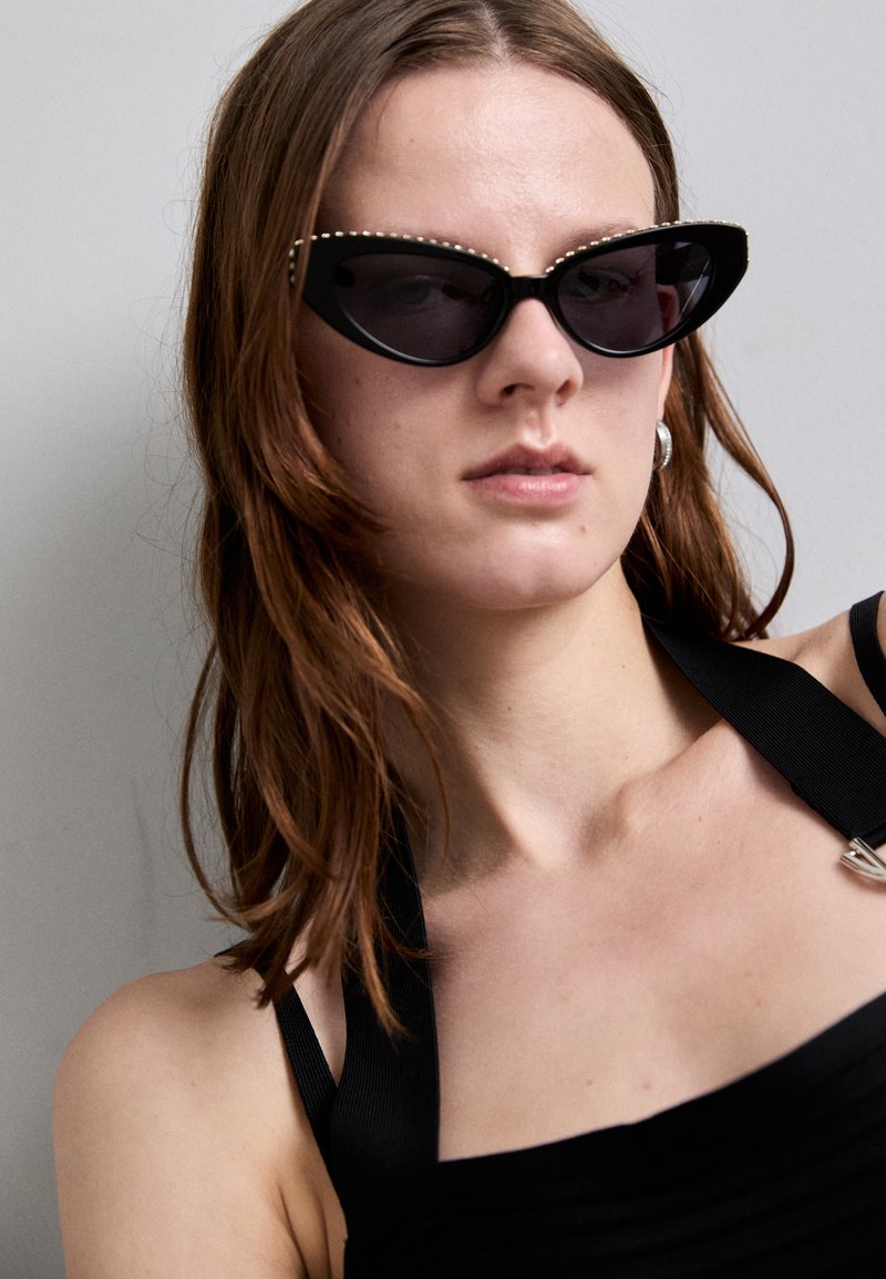 Black cat-eye sunglasses with dark lenses and rhinestone accents along the top edge, set against a neutral background.