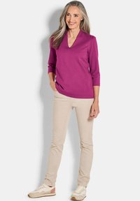 Fuchsia v-hals top met driekwart mouwen, gecombineerd met beige slim-fit broek en beige sneakers met lichtroze accenten.