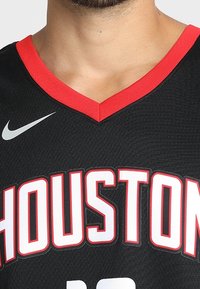 Czarna koszulka koszykarska z czerwonym dekoltem w kształcie litery V. "HOUSTON" jest wyraźnie wyeksponowane dużymi białymi literami. Logo Nike w kolorze szarym.