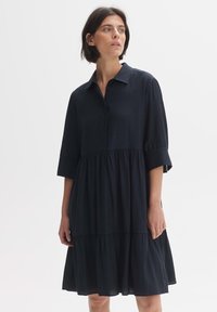 Dunkelblaues Hemdkleid mit Kragen, dreiviertellangen Ärmeln und gestuftem Rock. Der Stoff wirkt leicht und hat eine strukturierte Oberfläche.