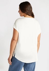 Weißes T-Shirt mit kurzen Ärmeln, entspannter Passform, abgerundetem Saum und Seitenschlitzen. Hergestellt aus weichem, leichtem Stoff.