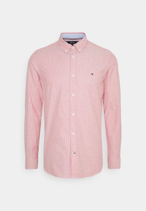Chemise rose à manches longues avec boutons, col boutonné et petit logo sur la poitrine gauche sur fond blanc.