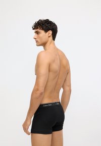 Czarne bawełniane bokserki z elastycznym paskiem w talii, z białym logo Calvin Klein, zaprezentowane na modelu z profilu bocznego.
