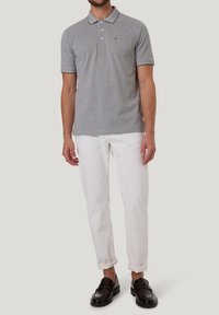 Grijze poloshirt met kraag, drie knopen, en borstzak, gecombineerd met opgerolde witte broeken en zwarte instapschoenen.