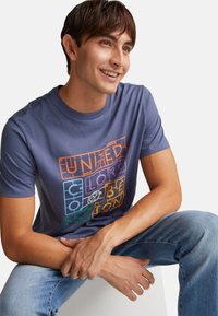 Camiseta de manga corta y cuello redondo de tejido azul claro con un diseño gráfico de texto multicolor en el frente. Textura suave y lisa.