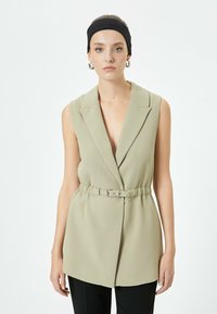 Ärmelloser, taillierter Blazer aus leicht olivgrünem Stoff mit tiefem V-Ausschnitt und strukturierten Revers. Glatte Textur und eine maßgeschneiderte Passform.