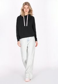 Hanorac negru cu şnururi roz pal, asortat cu blugi lejeri de culoare albastră deschisă şi adidaşi pastel, având un croi comod şi textură moale.