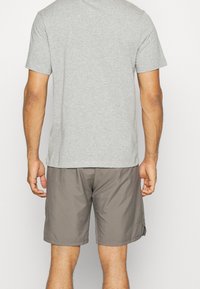 Camiseta gris de manga corta combinada con pantalones cortos gris claro, con un corte relajado. Los pantalones cortos tienen bolsillos laterales y un ligero brillo.