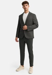 Ciemnoszary żakiet o slim fit, z klapami typu notch, oraz dwoma przednimi kieszeniami, w połączeniu z dopasowanymi spodniami slim oraz jasnobeżowymi sneakersami.