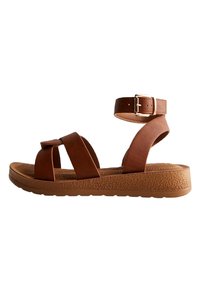 Sandales en cuir marron avec des sangles entrecroisées, boucle à la cheville et semelle en plateforme texturée. Design décontracté avec une construction confortable.