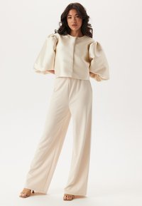 Cremefarvet cropped top med puffede ærmer, parret med vide bukser. Glat stof, minimalistisk design, ingen synlige mønstre eller metaldele.