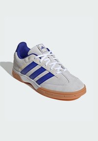 Light gray suede athletic shoe with blue stripes, white laces, and a gum rubber sole. Features a padded collar and logo on the tongue.