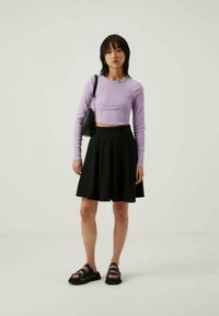 Levanduľový top s dlhým rukávom a skráteným strihom, čierna rozšírená sukňa po kolená, čierne sandále na remienky a malá čierna kabelka. Jednoduchý, priliehajúci dizajn.